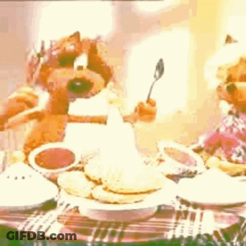 Two Teddy Bears Sitting At Table With Food And Spoon GIF