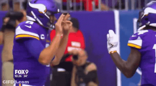 Two Vikings Football Players Are High Fiving Each Other On The Field GIF