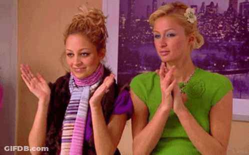 Two Women Are Clapping Their Hands In Front Of A Picture Of A City At Night . GIF