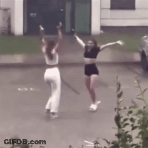 Two Women Are Dancing In A Parking Lot With Their Arms Outstretched GIF