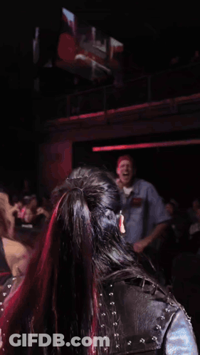 Two Women Are Dancing In Front Of A Crowd In A Dark Room With A Large Screen Behind Them GIF