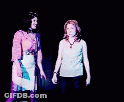 Two Women Are Dancing In Front Of A Microphone And One Has Her Arm In The Air GIF