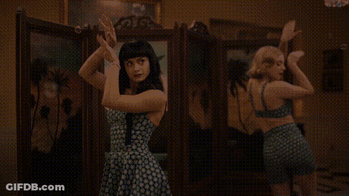 Two Women Are Dancing In Front Of A Mirror In A Room . GIF