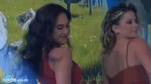 Two Women Are Dancing In Front Of A Painting That Says Vamos La Alegria GIF