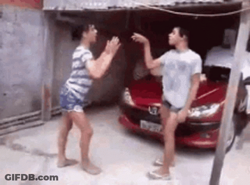 Two Women Are Dancing In Front Of A Red Car In A Parking Lot . GIF
