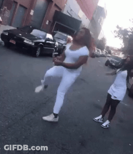 Two Women Are Dancing On The Street In Front Of A Black Car GIF
