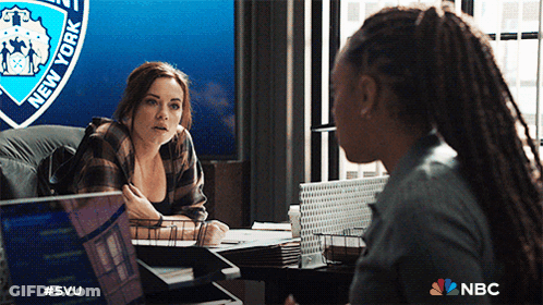 Two Women Are Having A Conversation In Front Of A New York Police Badge GIF