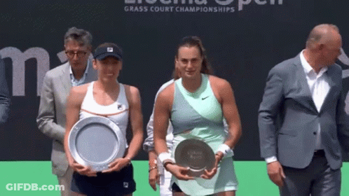 Two Women Are Holding Trophies In Front Of A Sign That Says Grass Court Championships . GIF
