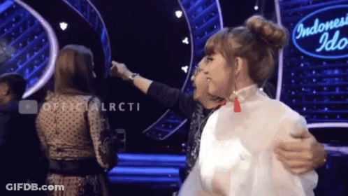 Two Women Are Hugging In Front Of An Indonesia Idol Sign GIF