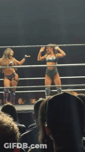 Two Women Are In A Wrestling Ring With Their Arms In The Air GIF