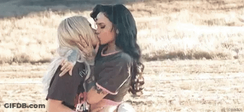 Two Women Are Kissing In A Field While Standing Next To Each Other . GIF