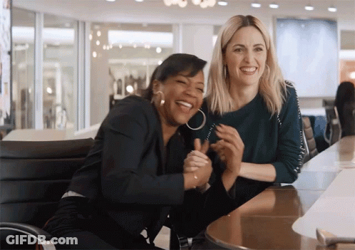 Two Women Are Laughing And Hugging Each Other While Sitting At A Table GIF