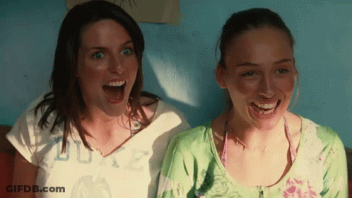 Two Women Are Laughing With One Wearing A Shirt That Says Duke On It GIF