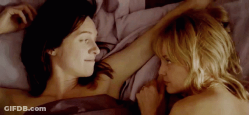 Two Women Are Laying In Bed Looking At Each Other And Touching Each Other 'S Arms . GIF