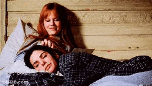 Two Women Are Laying On A Bed One Is Reading A Book GIF