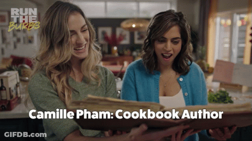 Two Women Are Looking At A Cookbook Titled Camille Pham GIF