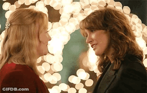 Two Women Are Looking Into Each Other 'S Eyes In Front Of Christmas Lights . GIF