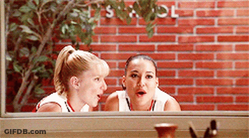 Two Women Are Looking Out Of A Window With A Brick Wall In The Background GIF