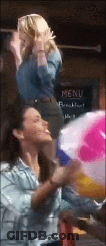 Two Women Are Playing With A Beach Ball In Front Of A Menu GIF