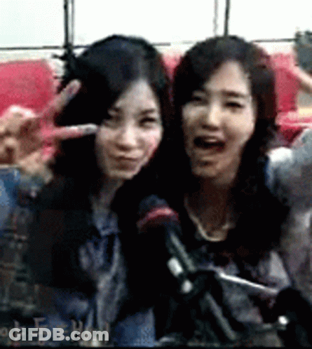 Two Women Are Posing For A Picture And One Is Making A Peace Sign GIF