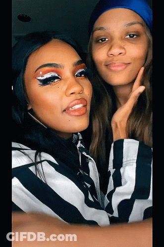 Two Women Are Posing For A Picture With One Wearing A Blue Hat GIF