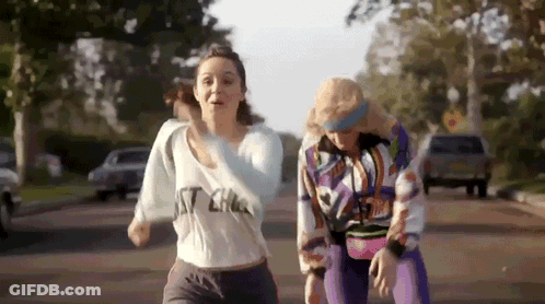 Two Women Are Running Down A Street With One Wearing A Shirt That Says ' I 'M A ' On It . GIF