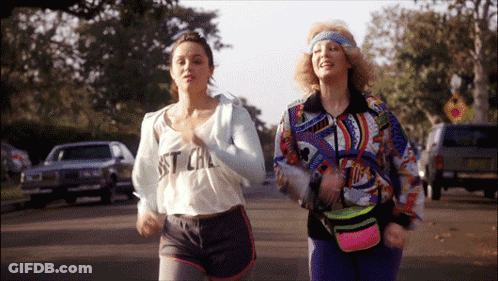 Two Women Are Running Down A Street With One Wearing A Shirt That Says Just Cal GIF