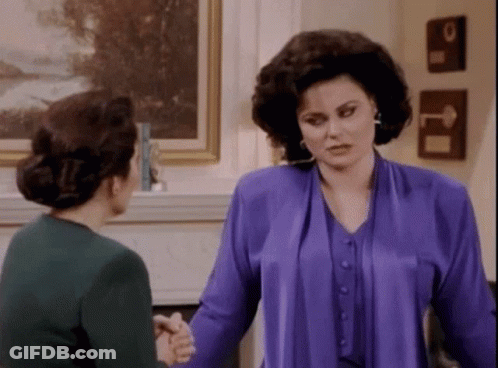Two Women Are Shaking Hands In A Living Room . GIF