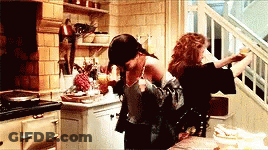 Two Women Are Sitting At A Table In A Kitchen Looking Out A Window . GIF