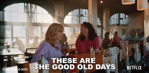Two Women Are Sitting At A Table In A Restaurant With The Words " These Are The Good Old Days " GIF