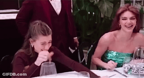 Two Women Are Sitting At A Table With Glasses Of Wine And Laughing . GIF