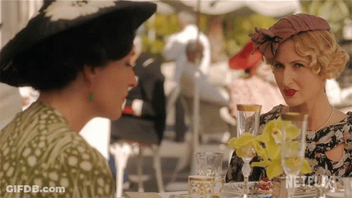 Two Women Are Sitting At A Table With Netflix Written On The Bottom GIF