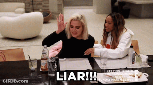 Two Women Are Sitting At A Table With The Word Liar Written On It GIF