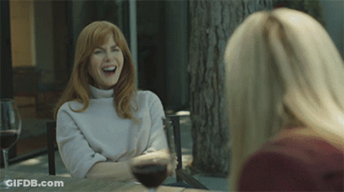 Two Women Are Sitting At A Table With Wine Glasses And One Is Laughing GIF