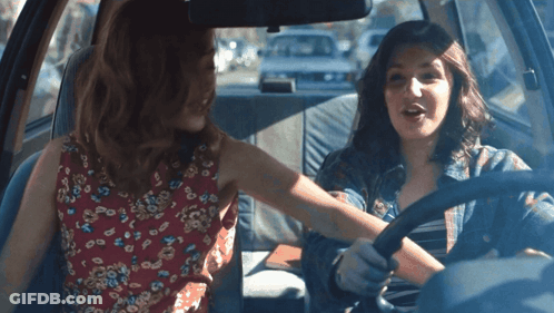 Two Women Are Sitting In A Car And One Is Wearing A Red Floral Dress GIF
