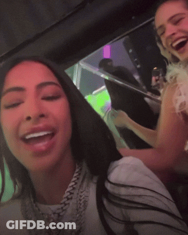 Two Women Are Sitting In A Car And One Is Wearing A White Shirt With A Chain Around Her Neck GIF