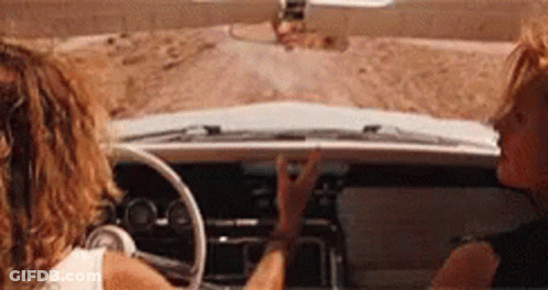 Two Women Are Sitting In A Car On A Dirt Road . GIF