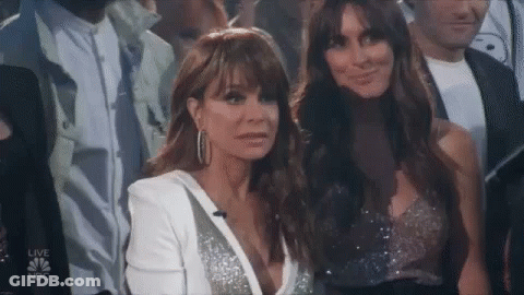 Two Women Are Sitting In A Crowd And One Is Wearing A White Jacket . GIF