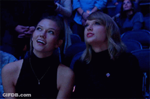 Two Women Are Sitting In A Stadium Looking Up At The Sky . GIF