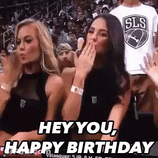 Two Women Are Sitting In The Stands At A Basketball Game And One Is Blowing A Kiss . GIF