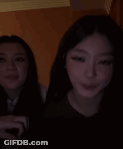 Two Women Are Sitting Next To Each Other In A Dark Room And Smiling . GIF