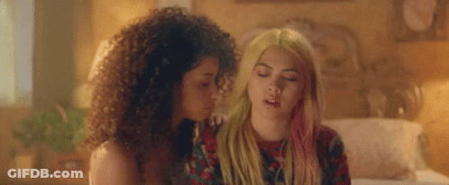Two Women Are Sitting Next To Each Other On A Bed . One Of The Women Has Pink Hair . GIF