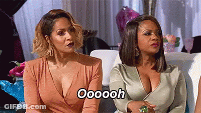 Two Women Are Sitting Next To Each Other On A Couch And One Of Them Is Wearing A Plunging Neckline Dress . GIF