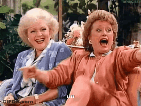Two Women Are Sitting Next To Each Other On A Couch Laughing And Pointing . GIF