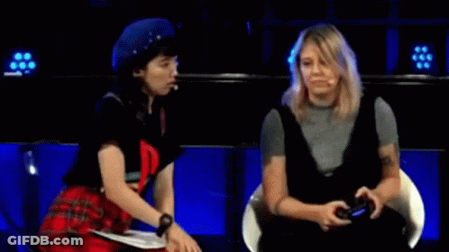 Two Women Are Sitting Next To Each Other On A Stage And One Of Them Is Holding A Video Game Controller . GIF