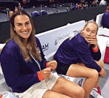 Two Women Are Sitting On A Bench With Pacific Tommy Written On The Wall Behind Them GIF