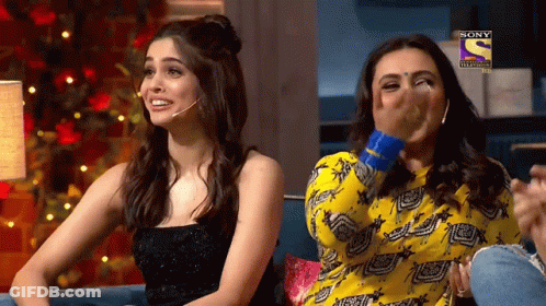 Two Women Are Sitting On A Couch And One Of Them Is Covering Her Mouth With Her Hand While The Other Is Laughing .. GIF