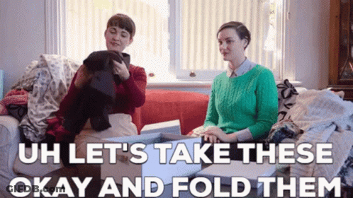 Two Women Are Sitting On A Couch Looking At Clothes And The Caption Says `` Let 'S Take These Okay And Fold Them '' GIF