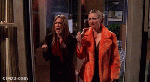 Two Women Are Standing In A Doorway With One Wearing An Orange Coat GIF