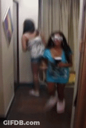 Two Women Are Standing In A Hallway Looking At Each Other GIF